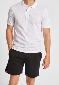 Short-sleeve white polo shirt with a classic collar and three buttons, paired with black fleece shorts featuring a small red logo.