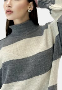Randig tröja i grått och kräm, med hög polokrage och ribbad textur. Silverfärgade stiftörhängen kompletterar outfiten.