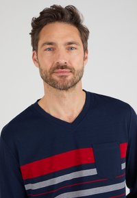Marineblauwe V-hals T-shirt met horizontale strepen in rood en wit. Voorzien van een borstzak en zachte katoenstof. Textuur is zichtbaar.