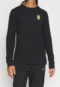 Langarmiges schwarzes Baumwoll-T-Shirt mit einem kleinen, mehrfarbigen Grafikdesign auf der Brust und einem Rundhalsausschnitt.