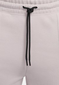 Pantalones deportivos gris claro con superficie texturizada, con cordón negro en la cintura y topes metálicos.