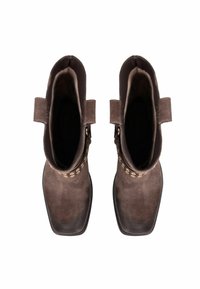 Bocanci scurți din suede maro, cu deschideri rotunde, detalii cusute și un design cu vârf pătrat. Include mânere la toc pentru o purtare ușoară.
