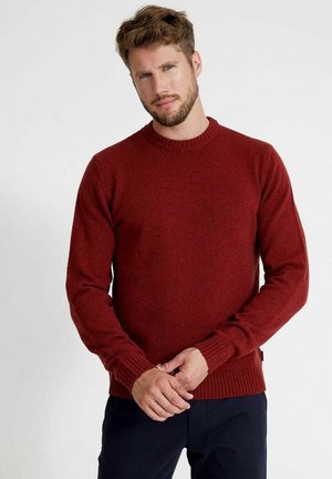 Czerwony sweter dzianinowy z okrągłym dekoltem, teksturową tkaniną, ściągaczami przy mankietach i dolnej krawędzi, noszony przez modela z krótkimi włosami i brodą na jednolitym tle.