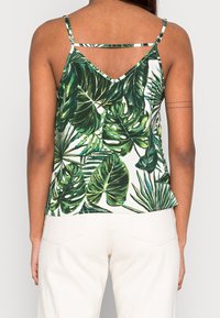 Top senza maniche con motivo di foglie tropicali verdi su sfondo bianco. Presenta spalline sottili e un orlo leggermente svasato. Tessuto morbido.