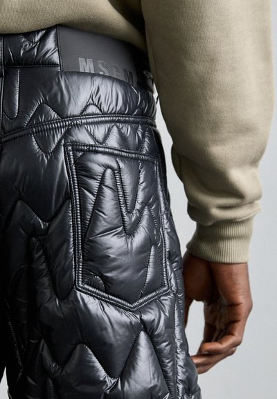 Padded schwarze Hose mit einem gesteppten Design, einer auffälligen Tasche und einem geprägten Bund mit "MSGM"-Logo. Glatte, glänzende Textur.