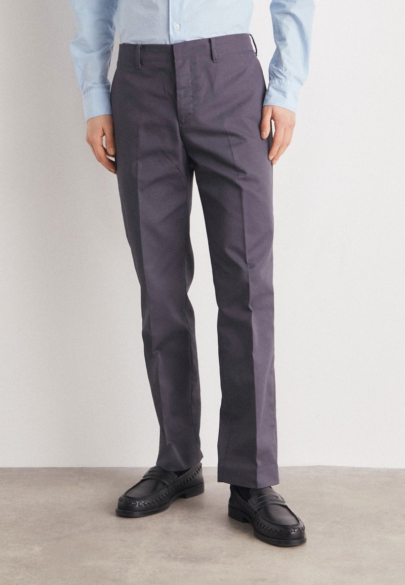 Chinos bleu marine à coupe droite, en coton, à plat devant, avec poches latérales et poches passepoilées arrière, associés à des mocassins noirs.
