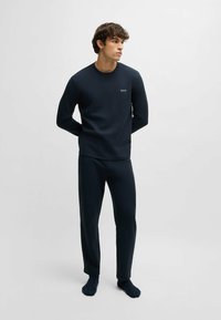 Donkerblauwe lange mouwen top en bijpassende broek van zacht materiaal. Heeft een aansluitende pasvorm en een klein logo op de borst. Casual loungewear.