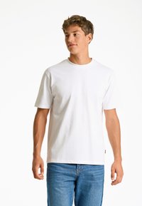 Vit bomullst-shirt med korta ärmar och rund halsringning, bärs med blå denimjeans. Mjuk struktur och avslappnad passform.