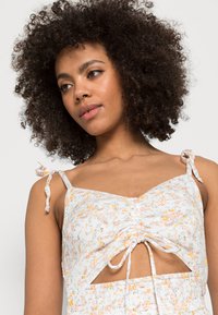 Camisola com padrão floral e franzido, feita de tecido leve, com laços ajustáveis nas alças, nas tonalidades de branco, laranja e verde.