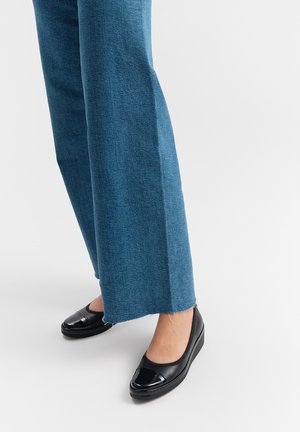 Black flat shoes with a glossy toe accent, paired with blue wide-leg denim jeans featuring raw hem details. Simple design, smooth texture.