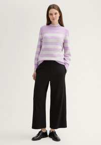 Lila und graue gestreifte Strickjacke mit hohem Kragen, kombiniert mit weiten schwarzen Hosen und schwarzen Schnürschuhen. Glatte Textur.