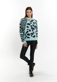 Lichtblauwe fuzzy trui met zwarte dierenprints en strepen. Gecombineerd met zwarte leren broek en veterschoenen in het zwart.