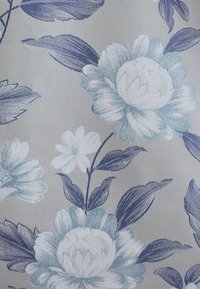 Bloemrijke stof met grote blauwe en witte bloemen tegen een gestructureerde grijze achtergrond. Details zijn groene bladeren en subtiele schaduwen.