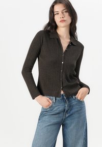 Brun ribbad kavaj med krage, långa ärmar och knappstängning. Matchad med ljusblå vida jeans, som visar en avslappnad passform.