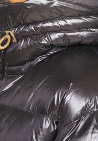 Chaqueta de plumas negra con un acabado brillante y texturizado, con secciones cosidas y un detalle de botón de madera en el cuello.