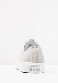 Grå canvas sneakers med vit gummisula, rund tå och logodetalj på hälen, med en enkel sydd design.