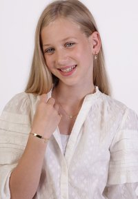 Gold jewelry includes a chain bracelet with a star charm and a delicate star pendant necklace. The subject wears a white textured blouse.