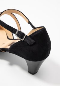 Sandal con tacco in suede nero con cinturino alla caviglia e fibbia argentata. Presenta una punta arrotondata e un tacco alto a forma affusolata. Sottopiede in pelle liscia.