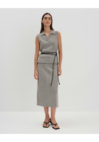 Vestito grigio senza maniche con scollatura a colletto, vita stretta con una cravatta nera e silhouette aderente lunga fino alla caviglia. Texture liscia.