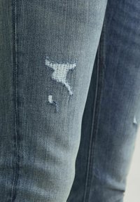 Jeans de denim azul claro con parches desgastados en las rodillas, presentando bordes deshilachados, un desvanecimiento sutil y un diseño ajustado.