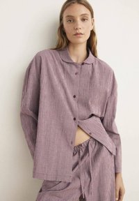 Rutig skjort- och byxdress i röd och vit bomull. Löst snitt, knappad krage och elastisk midja på byxorna.