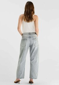 Jean large en denim gris clair avec une taille haute, doté de deux poches arrière et d'une coupe décontractée. Le modèle porte un débardeur blanc et des talons.
