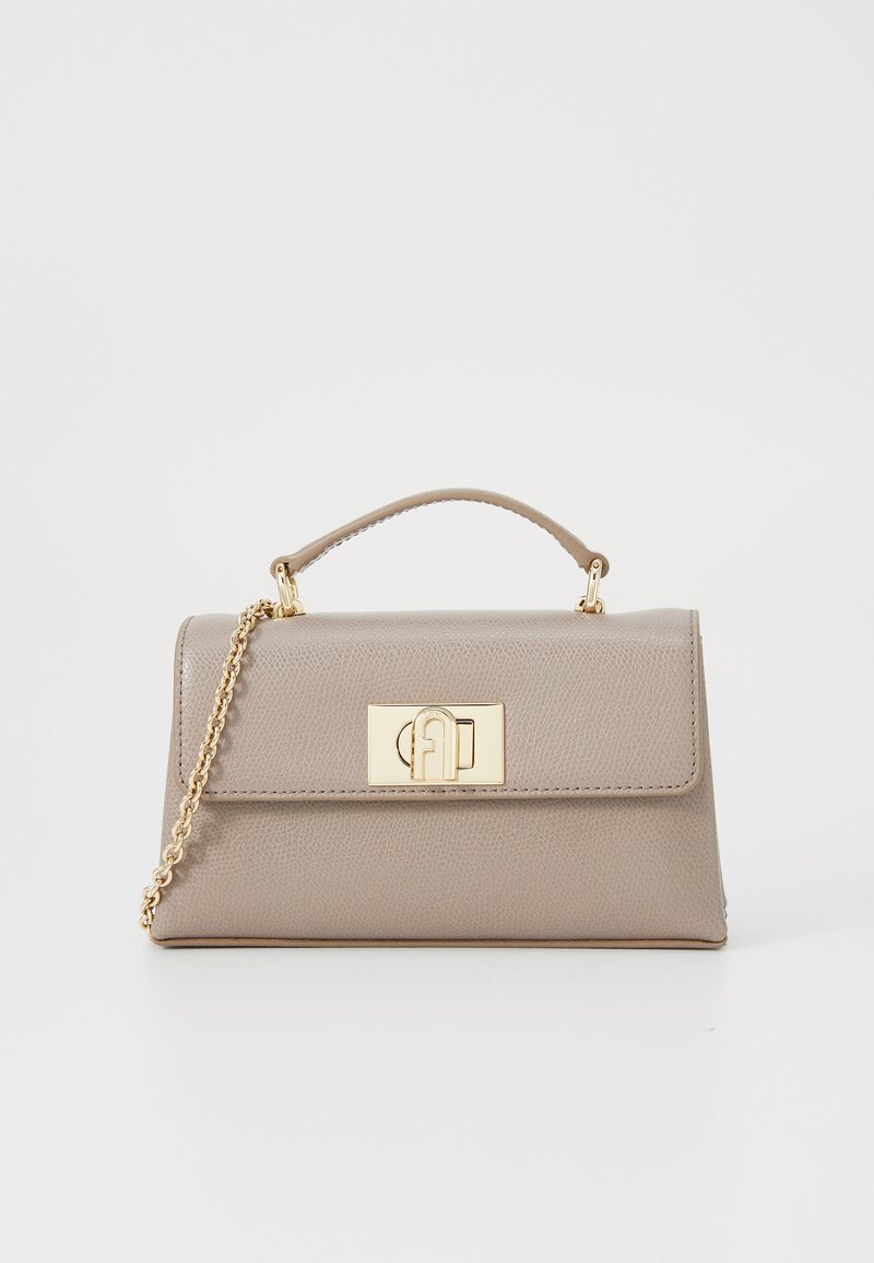 Bolsa de mão em pele bege com uma forma estruturada, ferragens douradas, uma pega superior e uma alça de corrente destacável. Apresenta uma aba com um fecho de logotipo.