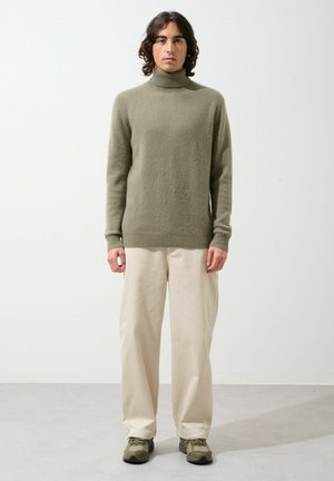 Pull vert olive à col montant, fabriqué en tissu doux. Associé à un pantalon beige ample et des baskets grises. Design simple et coupe décontractée.
