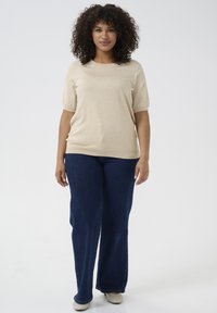 Beige knitted short-sleeve sweater, round neckline, paired with dark blue wide-leg jeans and light-colored shoes. Smooth texture, casual fit.