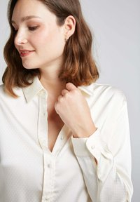 Chemise blanche à boutons en texture soyeuse avec un motif de points subtil, dotée d'un col classique et de poignets boutonnés.