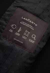 Czarna etykieta z białym tekstem, zawierająca informacje o typie tkaniny, komforcie cieplnym, elastyczności i dbałości o szczegóły, z ikoną mieszanki wełny.