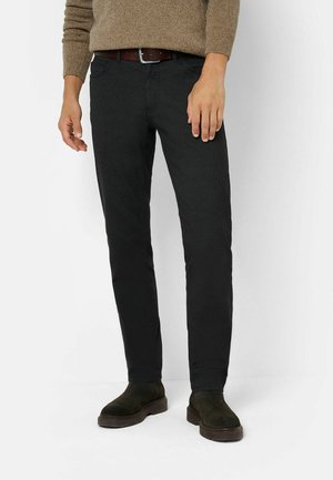 Schwarze Jeans im Slim Fit, aus strukturiertem Stoff, mit fünf Taschen und einem braunen Ledergürtel. Kombiniert mit dunkelgrünen Wildlederstiefeln.