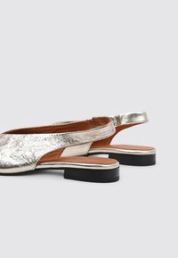 Zapatos slingback metálicos plateados con un upper texturizado, parte trasera abierta y una suela negra. Presentan una punta redondeada y un diseño minimalista.