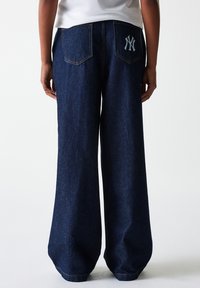 Jean large en denim foncé. Caractéristiques : deux poches arrière avec un logo blanc et un surcroît de couture contrasté le long des coutures.