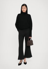 Melna, pārlieku liela turtlenecks adīta džemperis ar ribu aprocēm, teksturēti melni platāki bikses ar fringu apakšmalu un maza brūna rokas soma.