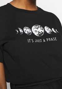 Camiseta de algodón negra con un gráfico blanco de fases lunares sobre el texto "SOLO ES UNA FASE" en una fuente sans-serif. Diseño de mangas cortas.