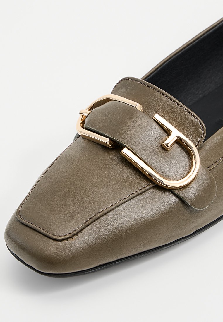 Mocassin en cuir vert olive avec un bout pointu, présentant une boucle dorée et une texture lisse. Doublure intérieure noire.