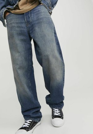 Losse blauwe denim jeans met een vervaagde afwerking, met wijde pijpen opgerold bij de manchetten, gecombineerd met zwart-witte sneakers.