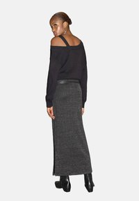 Svart off-shoulder tröja tillsammans med en lång, strukturerad, mörkgrå kjol med sidoficka. Modellen har på sig kraftiga svarta stövlar.