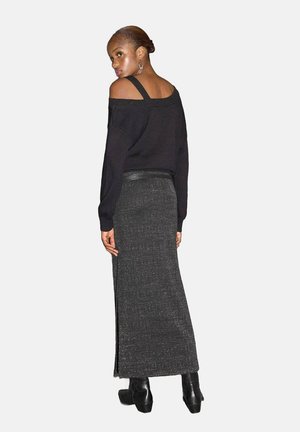 Zwarte off-shoulder trui gecombineerd met een lange, gestructureerde, donkergrijze rok met een zijsplit. Model draagt chunky zwarte laarzen.