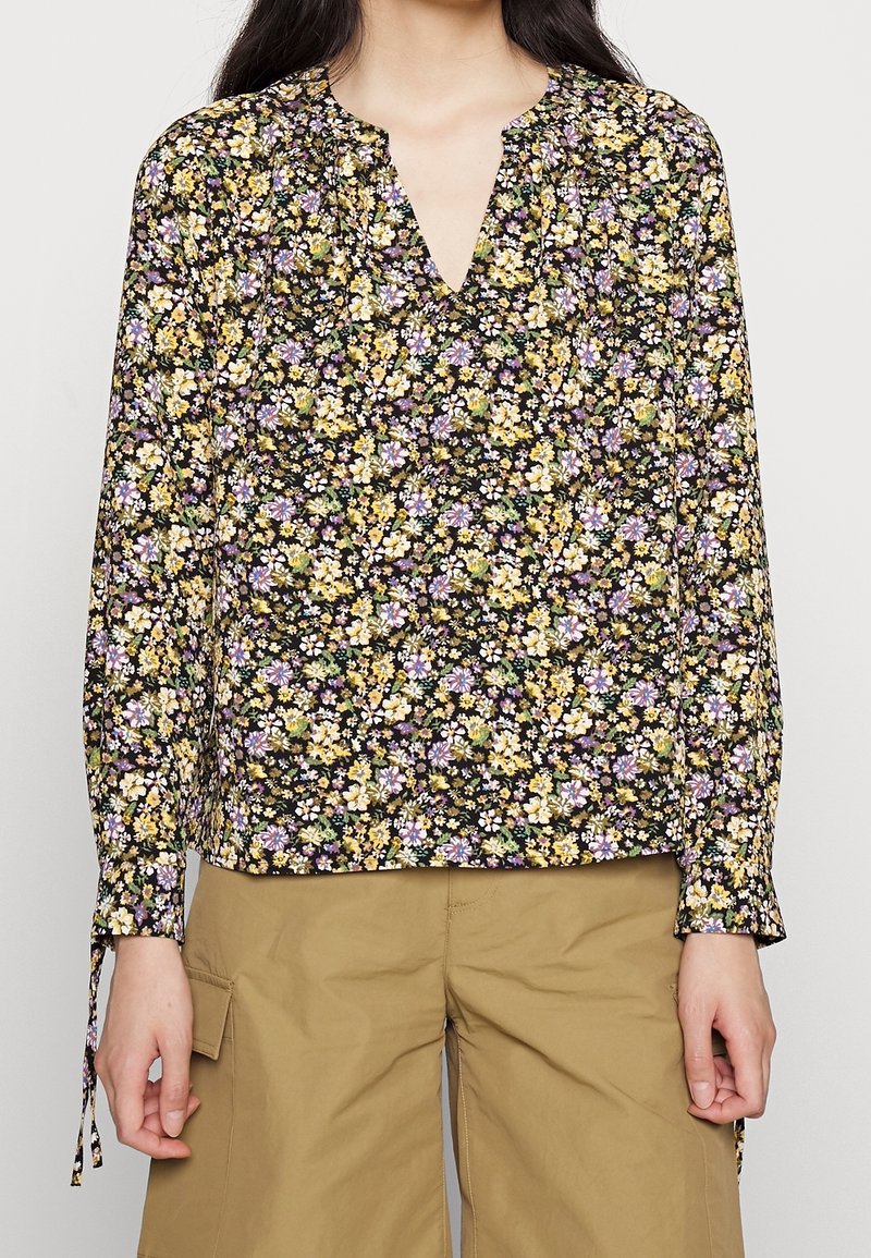 Blomsterlangærmet bluse med sort baggrund, der har gule, lilla og hvide blomster. V-hals og samlede ærmer med bindebånd.