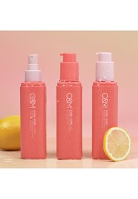Three pink hair product bottles with spray and pump tops, featuring droplets on the surface, positioned next to a sliced lemon.