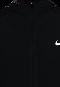 Veste noire avec une fermeture éclair centrale et un logo Nike blanc sur la partie droite de la poitrine.