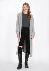 Längerer, grauer, flauschiger Cardigan über einem dunkelgrauen Oberteil, kombiniert mit schwarzen, kaputten Jeans und kniehohen schwarzen Stiefeln. Texturiertes, übergroßes Design.