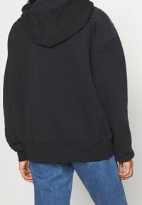 Svart hooded sweatshirt med en avslappnad passform, som har en mjuk textur, ribbade ärmar och kontrasterande tyg på axlarna.