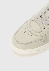 Zapatilla de cuero gris claro con punta redonda, detalles perforados, cordones grises y una suela de goma blanca contrastante. Diseño simple y de perfil bajo.