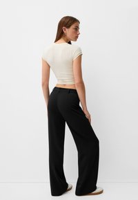 Cream short-sleeve crop top paired with high-waisted black trousers. Smooth fabric; relaxed fit; minimalistic design; subtle detailing.