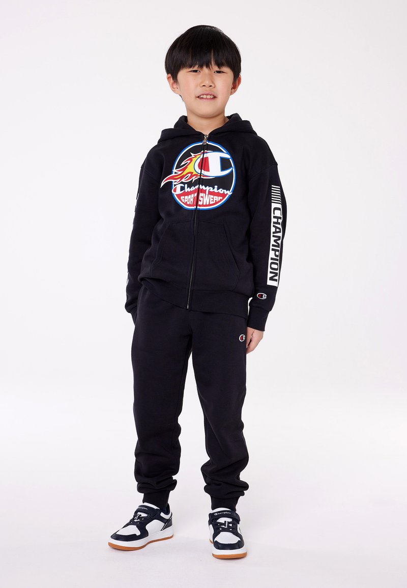 Set di felpa nera con cappuccio e pantaloni della tuta, con logo floreale sul petto, polsini elasticizzati e lettering bianco "Champion" sulle maniche.