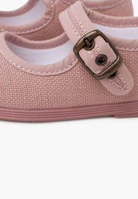 Zapatillas de lona rosa con un acabado texturizado, que presentan una puntera redondeada y una correa con un acento de hebilla de bronce. Forro blanco.