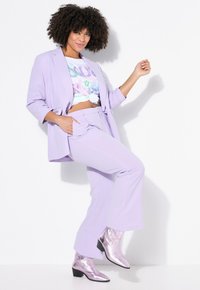 Lavendel pak met een ontspannen blazer en op maat gemaakte broek, gecombineerd met een grafisch crop top en metallic lavendelkleurige enkellaarzen.